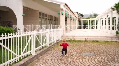 Little girl runs waving her hands on the paving stones near the pergola in the garden. High quality 4k footage