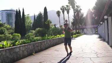 Dad with a little girl on his shoulders walks bouncing along a paved path in a green park. High quality 4k footage
