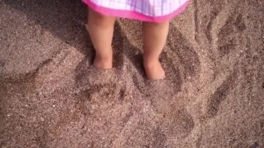 Little girl tramples her bare feet on the sand with small shells. High quality 4k footage