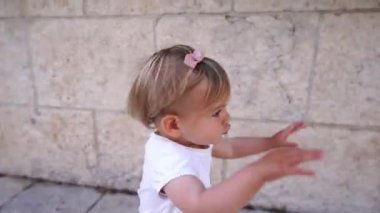 Little girl runs to the bench against the wall, balancing with her arms. High quality 4k footage
