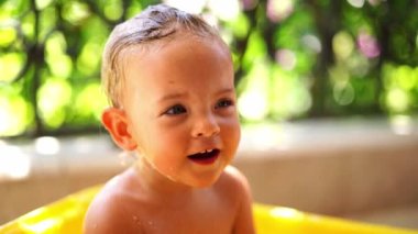 Little girl with wet hair sits in a bowl on the balcony and babbles. High quality 4k footage