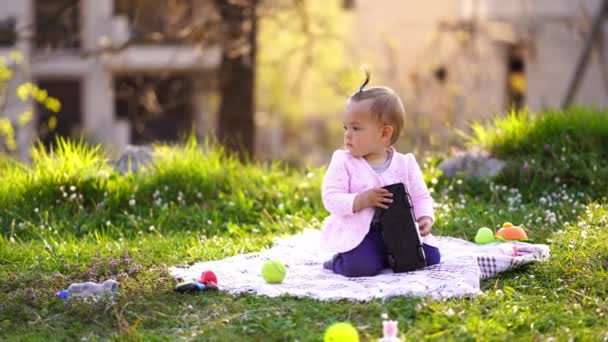 女の子はおもちゃの車で緑の芝生の上の毛布の上に座っています 高品質4K映像 — ストック動画