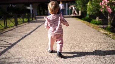 Little baby walks along the path to the gazebo. Back view. High quality FullHD footage