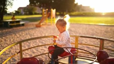 Mom spins a little girl on a carousel under the sunlight on the playground. High quality 4k footage