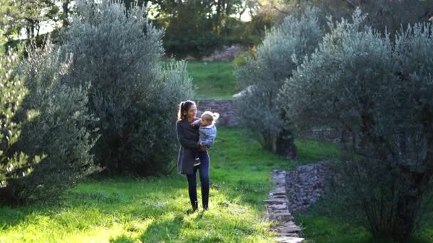 Mamá Con Una Niña Brazos Camina Por Parque Entre Árboles — Vídeos de Stock