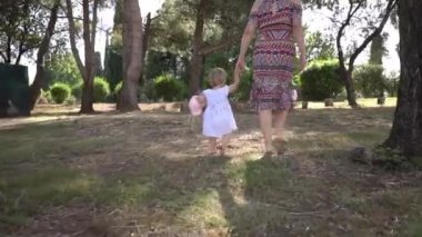 Mom and little girl walk barefoot on the green grass. Back, view. High quality FullHD footage