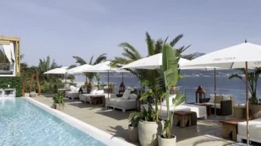 Double sun loungers stand under sun umbrellas around the pool with turquoise water. High quality 4k footage