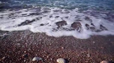 Beyaz sörf köpüğü renkli taşlı çakıl taşlı kumsalda yuvarlanıyor. Yüksek kaliteli FullHD görüntüler