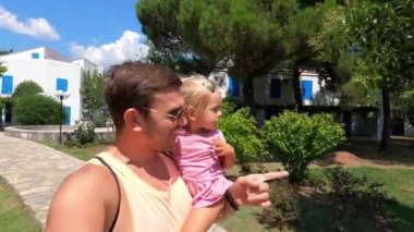 Dad with a little girl in his arms walks through the park and shows her the trees. High quality 4k footage