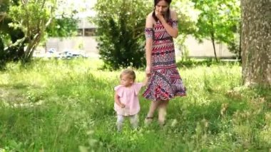 Mom walks with a little girl in the park, holding her hand. High quality FullHD footage