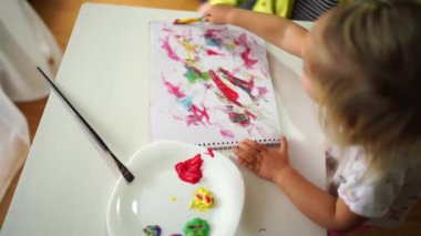 Little girl mixes paints with a brush and draws in an album. High quality 4k footage