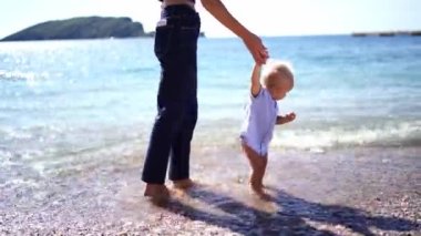 Mom leads a small baby by the hand on the sea surf. High quality 4k footage