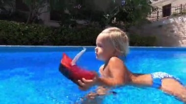 Little girl with a toy boat swims in the pool, supported by her dad hand. High quality 4k footage