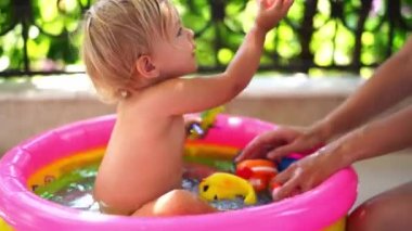 Mom plays with a little girl sitting in an inflatable pool with rubber toys. High quality 4k footage