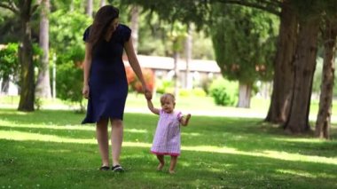 Little girl walks in the park by the hand with her mother and babbles. High quality 4k footage