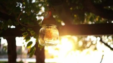 Jar lamp hangs from a wooden beam of a pergola in the rays of sunlight. High quality 4k footage