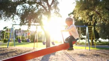Little girl swings on a swing-balancer and looks at a tree on the playground. High quality 4k footage