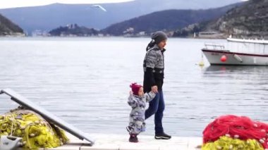 Mom with a small child walks along the pier holding hands past folded fishing nets. High quality 4k footage