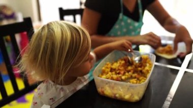 Little girl eats apple filling next to her mother sculpting buns. High quality 4k footage