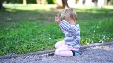 Little girl sits on her knees on a gravel path in the park and pokes her hands in the gravel. High quality 4k footage
