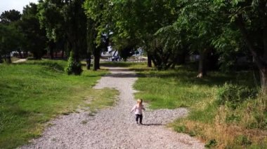 Little girl walks on a gravel path in a green park, balancing with her arms and staggering. High quality 4k footage