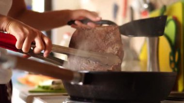 Kadın, elinde maşayla bir tavada dumanı üstünde biftek tutuyor. Yüksek kalite 4k görüntü