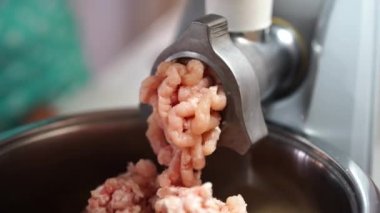 Pink pieces of minced meat fall out of the electric meat grinder into a bowl. High quality 4k footage