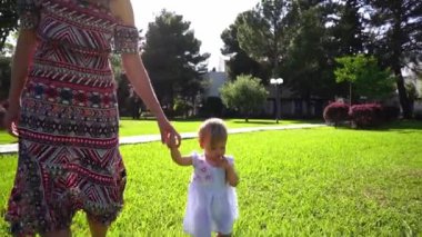 Annem, palmiye ağaçlarıyla dolu yeşil bir parkta küçük bir kızla el ele yürüyor. Yüksek kaliteli FullHD görüntüler