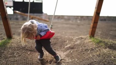 Little girl swings on a swing on her stomach and looks at the ground. High quality 4k footage