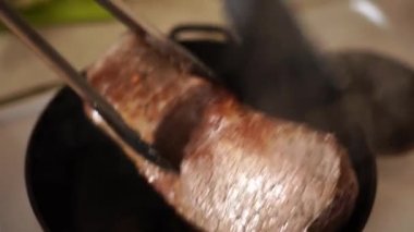 Bifteği bir tavada hazırlamak için spatula ve maşayla çevrildi. Yüksek kalite 4k görüntü