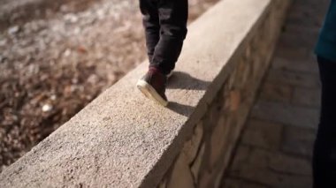 Small child runs along a stone fence on the beach next to his mom walking along the cobblestones. High quality FullHD footage
