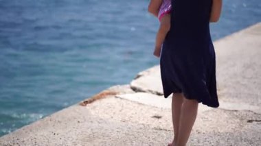 Mom with a little girl in her arms walks barefoot along the pier. Back view. High quality 4k footage