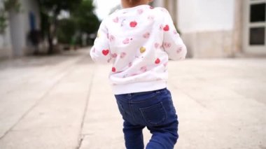 Little baby walks on tiles in the yard. Back view. High quality FullHD footage