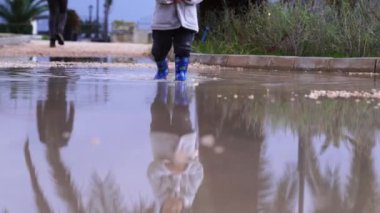 Little kid walks in rubber boots through the puddles in the park. High quality 4k footage