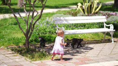 Little girl walks on the tiles barefoot to the cats sitting near the benches. High quality 4k footage