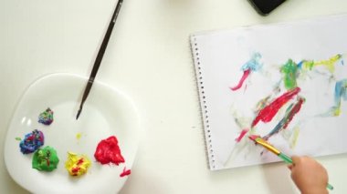 Küçük çocuk bir albümde boyalı fırçayla resim çizer. Yüksek kalite 4k görüntü