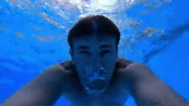 Young man swims underwater in the pool reflecting in the upper layers of the water. High quality 4k footage