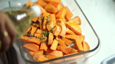 Woman pouring oil on sliced sweet potatoes with rosemary in a glass mold. High quality 4k footage