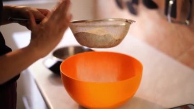 Woman sifts flour into a bowl through a sieve, slapping it. High quality 4k footage