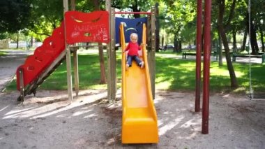 Little girl slides down the slide at the playground in the park. High quality 4k footage