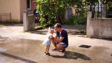 Little girl with her dad jump through the puddles in the yard. High quality 4k footage