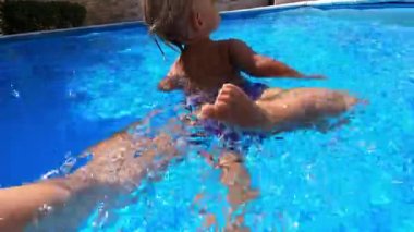 Little girl swims in the pool dangling her legs and arms with her dad support. High quality 4k footage