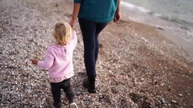 Little girl with her mother walk along the autumn beach holding hands. High quality FullHD footage