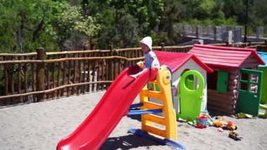 Panama şapkalı küçük kız renkli bir oyun parkında kaydırağın üzerinde oturuyor. Yüksek kalite 4k görüntü