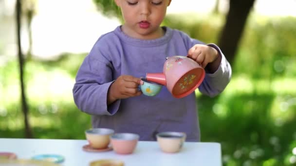 テーブルの上でおもちゃのカップとティーポットでお茶パーティーをしている女の子 高品質4K映像 — ストック動画
