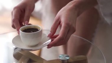 Bornozlu gelin masadan bir fincan kahve ve çay tabağı alıyor. Yüksek kaliteli FullHD görüntüler