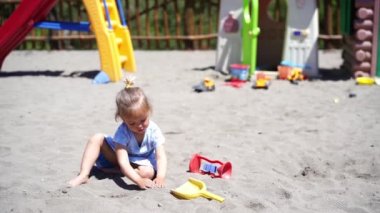 Küçük kız oyun parkındaki kumda oyuncak bir kürekle çukur kazıyor. Yüksek kalite 4k görüntü