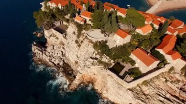 Kayalık Sveti Stefan adasındaki ağaçların arasında kırmızı çatıları olan eski evler. Yüksek kalite 4k görüntü