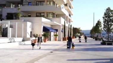 Küçük kız, annesinin önünde otelin arka planına karşı gezinti alanında yürüyor. Yüksek kalite 4k görüntü