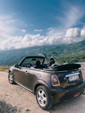 Üstü açık Mini Cooper dağların tepesinde bir kır yolunda duruyor. Yüksek kalite fotoğraf